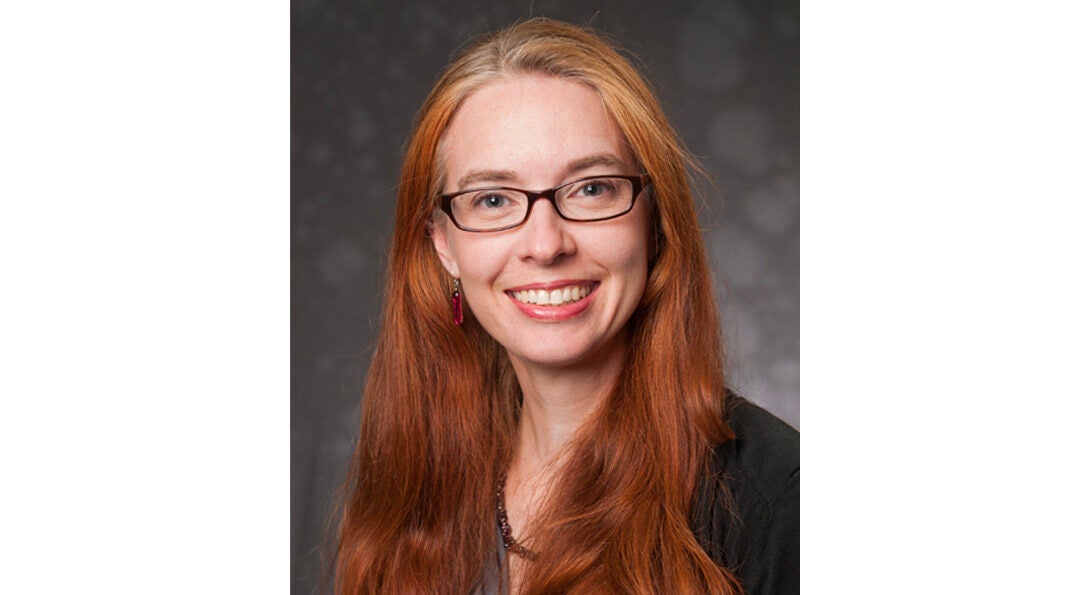 Portrait of Tina Griffin smiling, wearing glasses and a beaded necklace and a dark suit.